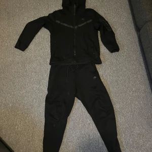 Nike tech - Säljer en Nike tech tracksuit på grund av den bara ligger och ej kommer till användning. Tracksuiten är i helt okej skick. De ända defekterna är att den är nopprig på baksidan av hoodien och byxorna och ett hål som sytts igen vid byxorna men som inte märks mycket.