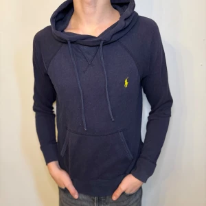 Marinblå Ralph lauren hoodie gul pony logga  - En tvärfet marinblå Ralph Lauren hoodie, gul pony logga, tröjan har även små klippningar på sidorna, de ska vara där och var där när jag köpte de från Ralph Lauren skulle säga att materialet är lite lite tunnare än en ”vanlig hoodie” | storlek XS, 42cm axelbredd, 54cm full längd, 49cm ärmlängd, måtten är ej helt exakta | sparsamt använd, skick 8,5-10 | vi postar alltid inom 24 timmar efter köp | skriv för fler bilder,  eller andra frågor //HLselling