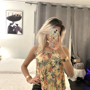 Blommig ärmlös topp - Säljer en somrig blommig topp i ljusa färger med ett härligt mönster av blommor och blad. Toppen är ärmlös och har en luftig passform, perfekt för varma dagar. Den har en mjuk och bekväm känsla.