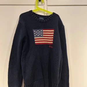 Mörkblå stickad tröja från Polo Ralph Lauren - Säljer en mörkblå stickad tröja från Polo Ralph Lauren med en amerikansk flagga broderad på framsidan. Ny pris=2000 Mitt pris=899. Mvh milo 