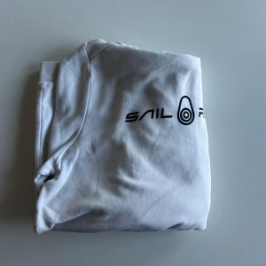 Vit hoodie från Sail Racing - Säljer en vit hoodie från Sail Racing med svart logotyp på bröstet. Tröjan har en klassisk design med långa ärmar och en praktisk känguruficka framtill. Priset är inte hugget i sten och hör av er vid minsta fundering!