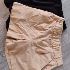 Beige och svarta shorts från lager 157 - Säljer ett par stilrena shorts i beige och svart från lager 157. De beige shortsen har en högmidjad design med elastisk midja och diskreta bakfickor. Perfekta för en avslappnad sommarlook. De svarta shortsen är också elastiska i midjan och passar bra till olika tillfällen.