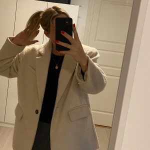 Creme-vit  kort kappa från Gina Tricot - Säljer en stilren oversized creme-vit kappa från Gina Tricot i storlek S. Den har en klassisk design med knappar framtill och två fickor. Perfekt för att hålla stilen i kyligare väder.