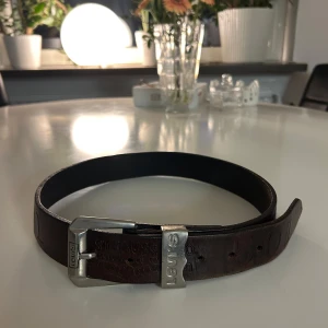 Brunt skärp från Levi's - Snyggt brunt skärp från Levi's i skinn med en robust silverfärgad spänne. Perfekt för att ge en stilren touch till din outfit. Skärpet har en klassisk design med Levi's-logga på spännet.