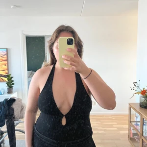 Svart halterneck body - Snygg svart halterneck body med djup urringning och en liten öppning framtill. Bekväm och stilren design.