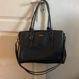 Svart axelväska från Don Donna - Snygg svart axelväska från Don Donna i syntetmaterial. Väskan har dubbla handtag och en justerbar axelrem. Den är rymlig med flera fack och stängs med dragkedja. Perfekt för att hålla ordning på dina saker. Perfekt till skola då den får plats med jätteeee mycket❤️ se bild 3 lite slitet❤️