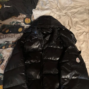 Svart pufferjacka  - Säljer en varm skön svart pufferjacka bra till hösten och vintern,har bara använt den tre gångar, den känns som en moncler Maya jacka. Den relativt liten i storleken, men den saknar två knappar på ärmen som man ser på bild tre. Jag har inte riktigt koll på varumärket.
