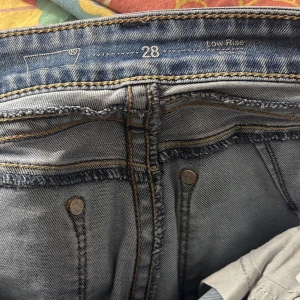 Blå jeans med låg midja från Levis  - Säljer ett par klassiska blå jeans med låg midja. De har en rak passform och är i storlek w28. Jeansen har de ikoniska bakfickorna med sömmar och är perfekta för en avslappnad stil.