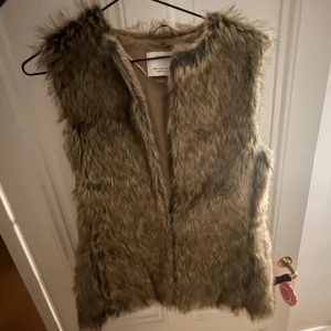 Brun pälsväst från Bershka - Säljer en snygg brun pälsväst från Bershka. Västen är perfekt för att ge en trendig touch till din outfit. Den är mjuk och har en naturlig look som passar bra till olika stilar.
