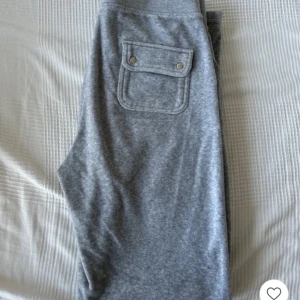 Grå mjukisbyxor från Juicy Couture - Snygga grå mjukisbyxor från Juicy Couture med snörning i midjan och praktiska fickor både fram och bak. Perfekta för en avslappnad stil. Byxorna har en mjuk och bekväm känsla.