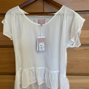 Vit blus, strl XS, InWear - Luftig, vit blus från InWear med korta ärmar, rund halsringning och volangdetalj i nederkant. 70% bomull, 30% siden. Helt ny, prislapp kvar med nypris 900kr.