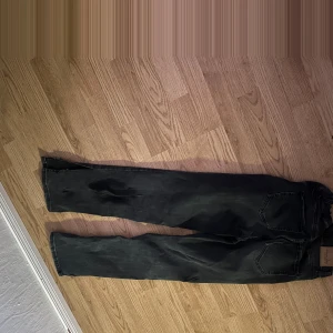 Svarta jeansbyxor - Snygga svarta jeansbyxor med en klassisk design. De har en rak passform och är utrustade med knappar och dragkedja framtill. Perfekta för en stilren look.