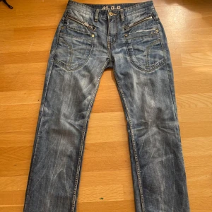 Blå jeans från M.O.D - Snygga blå jeans från M.O.D med en klassisk femficksdesign och slitna detaljer. De har en lite baggy passform och är utsvängda där nere. Jeansen har en knappgylf och är tillverkade i ett robust denimtyg. Midjemåttet är 88.