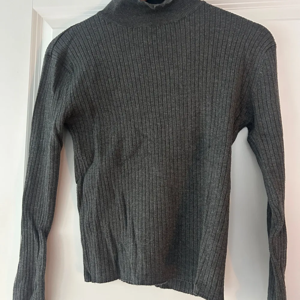 Säljer en stilren grå ribbad polotröja från Zara. Tröjan har en tight passform och långa ärmar, perfekt för kyligare dagar. Den är tillverkad i ett mjukt material som ger en bekväm känsla. Passar utmärkt till både jeans och kjol.. Neuletakit & Villapaidat.