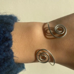 Armband silver - Unik armring i silverfärg med en elegant spiraldesign. Den öppna formen gör den justerbar och lätt att bära. Perfekt för att ge en stilren touch till din outfit. -stål -justerbar