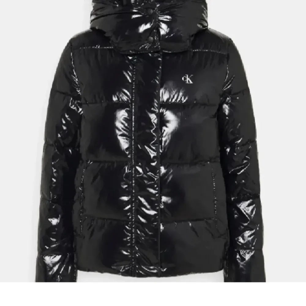 Snygg svart glansig dunjacka från Calvin Klein med huva och dragkedja. Jackan har en pufferdesign och CK-logga på bröstet. Köptes innan vintern nypris-ca 2100 beroende på sida. Storlek S. Takit.
