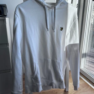 Vit Lyle & Scott hoodie - Säljer en stilren vit hoodie från Lyle & Scott med en liten broderad logotyp på bröstet. Tröjan har en klassisk design med spänne i huvan och en stor ficka framtill. Perfekt för en avslappnad look.  Hör av er vid intresse/frågor!