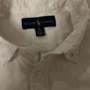 Vit skjorta från Ralph Lauren - Säljer en klassisk vit skjorta från Ralph Lauren med broderad logga på bröstet. Skjortan har långa ärmar och knappar framtill samt vid kragen. Perfekt för en stilren look. Pris kan diskuteras