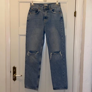 Blå jeans med slitningar - Snygga blå jeans med slitningar på knäna. De har en klassisk femficksdesign och en rak passform. Perfekta för en avslappnad stil. Dom är lite slitna längst ner på benen. 