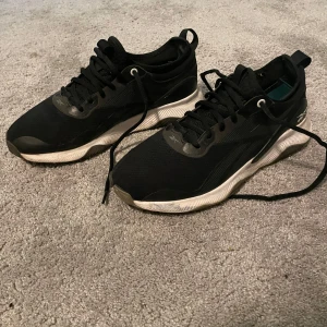 Svarta sneakers från Reebok - Snygga svarta sneakers från Reebok med vit sula och klassisk snörning. Perfekta för en sportig look eller vardagsbruk. Skorna har en stilren design med diskreta detaljer och en bekväm passform.