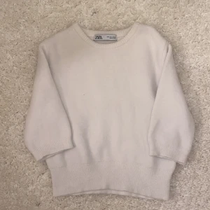 Vit tröja från Zara - Säljer en stilren vit tröja från Zara. Den har en enkel design med ribbade muddar vid ärmslut och nederkant. Perfekt för en minimalistisk look.