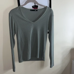 Grön ribbad tröja från 157 - Säljer en stilren grön ribbad tröja från 157. Tröjan har en v-ringad hals och långa ärmar, perfekt för en avslappnad look. Passar bra till både jeans och kjol. Perfekt för höst och vår!