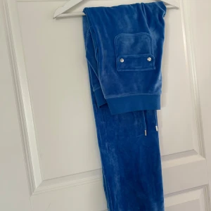 Blå mjukisbyxor från Juicy Couture - Snygga blå velourbyxor från Juicy Couture. Byxorna har en bekväm resårmidja med snörning samt praktiska fickor framtil samt två  bakfickor med knappar som är en sjukt snygg detalj! De perfekta bekväma snygga mjukisbyxorna! Dem är i färgen regatta och original priset för dessa är 1200kr. Byxorna är i mycket fint skick samt sparsamt använda, säljer för 700kr. Om man är intresserad av att köpa hela setet, har jag tröjan i strl M. Kan köpas tillsammans med byxorna för 1200kr. (Original pris 2500kr)🩷