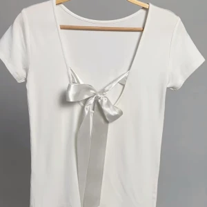 Vit kortärmad topp med knytband - Snygg vit topp med korta ärmar och en v-ringad design. Toppen har ett knytkand på baksidan. 