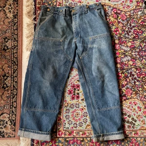 Blå jeans från Carhartt - Säljer ett par coola blå vintage jeans från Carhartt. De har en loose fit och är perfekta för en avslappnad stil. Byxorna har flera praktiska fickor och är gjorda i slitstarkt denim. Perfekta för både vardag och arbete. De är i bra skick och redo för nya äventyr! Midjemått: 49 innermått: 72.5.