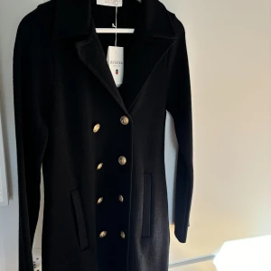 Helt ny kappa/kofta från busnel i storlek 36. - Säljer denna jättefina kofta/kappa från busnel. Man kan ha den som kappa utomhus om det är varmare ute men den fungerar lika bra att ha som kofta inomhus. Är helt ny och aldrig använd. 