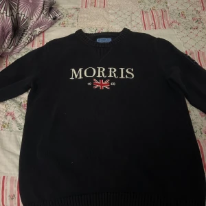 Mörkblå tröja från Morris - Säljer en snygg mörkblå tröja från Morris med broderad text och brittisk flagga på framsidan. Tröjan är i mycket bra skick och har en ribbad v-ringning samt muddar. Perfekt för höst och vinter! Pris kan diskuteras vid snabb affär