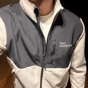 Vit/svart fleecejacka från HALO - Säljer en snygg vit/svart fleecejacka från HALO i storlek L. Jackan är köpt i Danmark 2022 och är helt oanvänd. Väldigt bekväm och varm som passar perfekt i kalla förhållanden. 