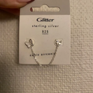 Silverörhängen med fjärilskedja från Glitter - Snygga örhängen i sterling silver 925 från Glitter. De har en fin fjärilsdesign med cubic zirconia och är sammanlänkade med en tunn kedja. Perfekta för att styla med att sätta i två hål långt ifrån varandra, köpta för 130 kr helt nya med originalförpackning.