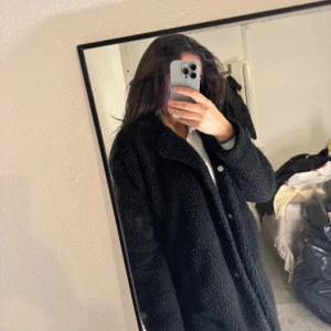 Svart teddyjacka - Mysig svart teddyjacka perfekt för kyliga dagar. Den har en avslappnad passform och långa ärmar, vilket gör den idealisk för både höst och vinter. Jackan är i mycket bra skick och har en stilren design som passar till det mesta. Perfekt för att hålla sig varm och snygg!
