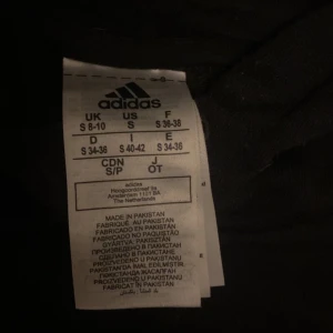 Svart hoodie från Adidas - Säljer en svart hoodie från Adidas i storlek S. Den har de klassiska vita ränderna längs ärmarna och Adidas-loggan på bröstet. Perfekt för en sportig look eller bara för att chilla hemma. Superbekväm och stilren! Lite Croppad så sitter lite ovanför byxorna 