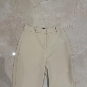 Beige kostymbyxor från Zara - Säljer ett par stilrena beige kostymbyxor från Zara i storlek S. Byxorna har en klassisk design med hög midja och raka ben, perfekt för både kontoret och festligare tillfällen. Tillverkade i ett bekvämt material som ger en snygg passform. Passar perfekt till höst- och vårgarderoben!
