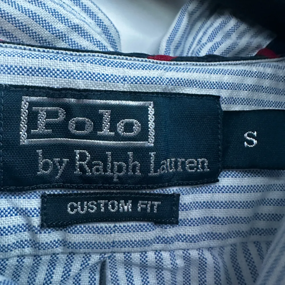 Säljer en snygg och klassisk randig skjorta från Polo Ralph Lauren i storlek S. Skjortan är blå och vit med långa ärmar och knappar framtill. Perfekt för både vardag och festliga tillfällen. Den har en broderad logga på bröstet som ger en extra touch av stil. Passar perfekt till jeans eller chinos!. Skjortor.