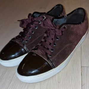 Vinröda Lanvin - Säljer ett par snygga Vinröda sneakers från Lanvin i mocka. De har en cool kombination av material med glansiga detaljer på tån och snörning i matchande färg. Perfekta för både vardag och fest! 🏆Snörerna är från ett par valentino flycrews, där dem är snyggare än det vanliga svarta! Dem är i Storlek UK-10 som motsvarar mot EU-44. Dem har 3 små defekter dåk, om man vill ha bild på dem så är det bara att medela! Jag säljer dessa för 1500 men kan tyvärr inte gå ner🙌🍾💯