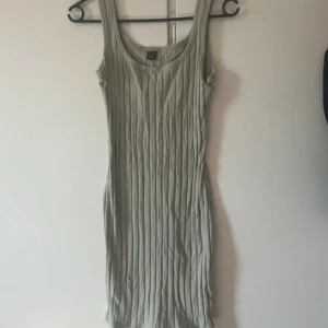 Grön ribbad klänning - Säljer en snygg grön ribbad klänning i mycket bra skick. Den är ärmlös och har en tight passform som framhäver figuren. Perfekt för både vardag och festliga tillfällen. Klänningen är gjord av ett mjukt och stretchigt material som gör den bekväm att bära hela dagen.