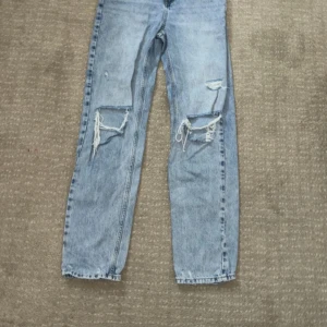 Ljusa jeans från Gina Tricot - Säljer ett par ljusa jeans från Gina Tricot i storlek 164. De har en cool, sliten look med revor på knäna och en straight passform. Perfekta för en avslappnad stil!