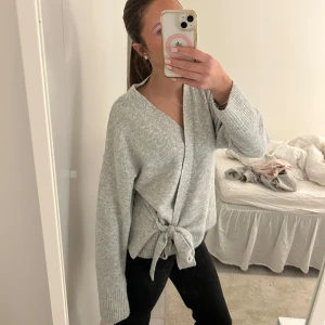 Grå stickad kofta med knyt - Säljer en supermysig grå stickad kofta i mycket bra skick. Den har långa ärmar och en snygg knytning framtill som ger en fin passform. Perfekt för höst och vinter när du vill hålla dig varm och stilren. Passar både till vardags och lite finare tillfällen. 🧶✨