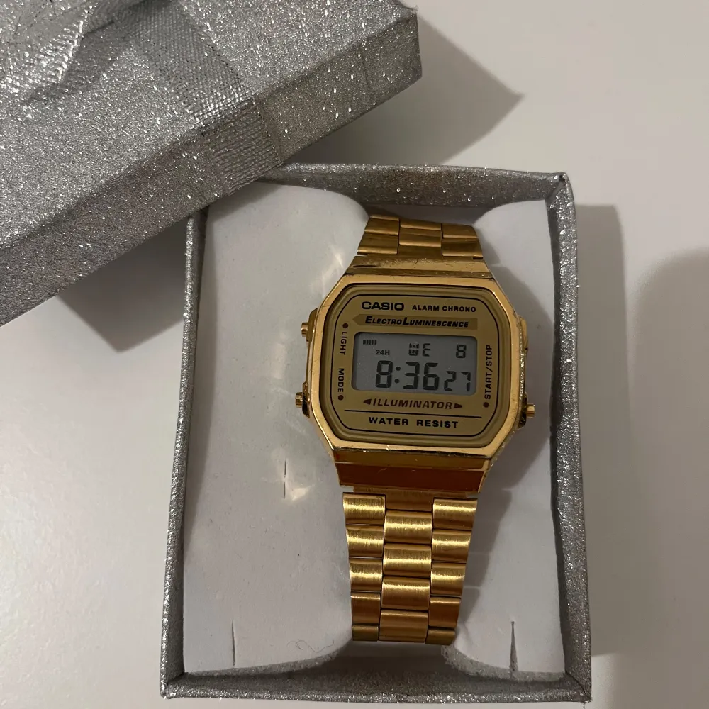 Säljer en snygg guldfärgad digital klocka från Casio. Den har en klassisk design med en fyrkantig urtavla och en länkarmband i metall. Klockan har funktioner som alarm, kronograf och belysning. Perfekt för både vardag och fest! 💛. Accessoarer.