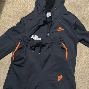 Säljer en svart Nike Air Max tracksuit med coola orange detaljer. Den har en dragkedja framtill och en huva för extra stil och skydd. Perfekt för höst och vår, och funkar lika bra till träning som till vardags. Tracksuiten är i mycket bra skick och redo för nya äventyr! 🖤🧡