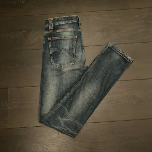 Nudie jeans - Säljer ett par snygga blå jeans från Nudie Jeans. Storleken är W28 L32 och de är slim i passformen. Nypris runt 1500 och de är i bra skick med några missfärgningar runt knävecken.