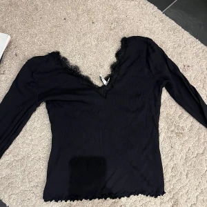 Svart långärmad topp med spetsdetaljer - Snygg svart topp med långa ärmar och v-ringning dekorerad med spets. Perfekt för både vardag och fest. Materialet känns mjukt och bekvämt mot huden.