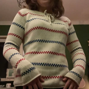Randig ribbad tröja från Tommy Hilfiger - Säljer en superfin ribbad tröja från Tommy Hilfiger i vitt med ränder i rött och blått. Den har långa ärmar och en söt knytning vid halsen. Perfekt för höst och vår! 