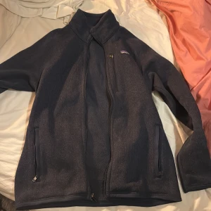 Mörkblå fleecejacka från Patagonia - Säljer en mörkblå fleecejacka från Patagonia i mycket bra skick. Jackan har en dragkedja framtill och två praktiska fickor med dragkedjor. Perfekt för kyliga höst- och vårdagar. Den är supermjuk och bekväm, idealisk för både vardag och friluftsliv.