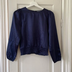Blå glansig blus - Super fin glansig blus från Grunt. Blusen är i barnstolen L skulle säga att den är ungefär 146-152. Superfint skick och är knappt använd. 