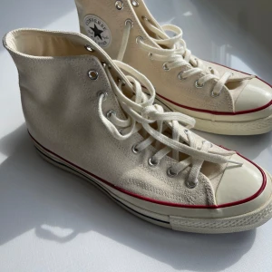 Converse Chuck 70 High - Nästan Nya! - Säljer ett par ikoniska Converse Chuck 70 High sneakers i färgen off-white. Skorna är i storlek 43 och har endast anänts en gång, vilket gör att de är i nästintill nyskick. Perfekt för den som vill ha ett par klassiska och bekväma sneakers.