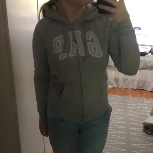 Grå hoodie från GAP - Säljer en grå hoodie från GAP i storlek XS. Har en fläck på ena ärmen, syns i bild 4. Är utöver det i bra skick. Nypris 589kr